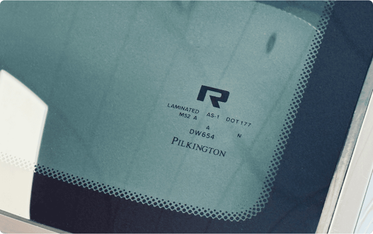 Close-up of a Revology branded Pilkington laminated windshield showing the "R" logo and DOT 177 safety certification markings.