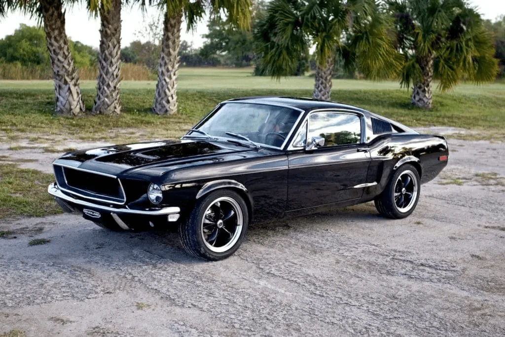 Black 1968 Revology Mustang GT Fastback parked near palm trees in a front three-quarter view.