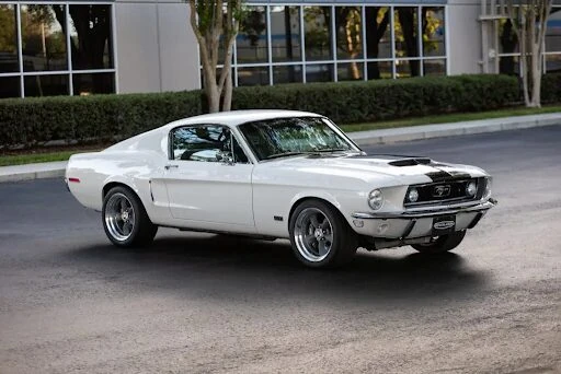 White 1968 Revology Mustang GT Fastback parked on a road in a front three-quarter view.
